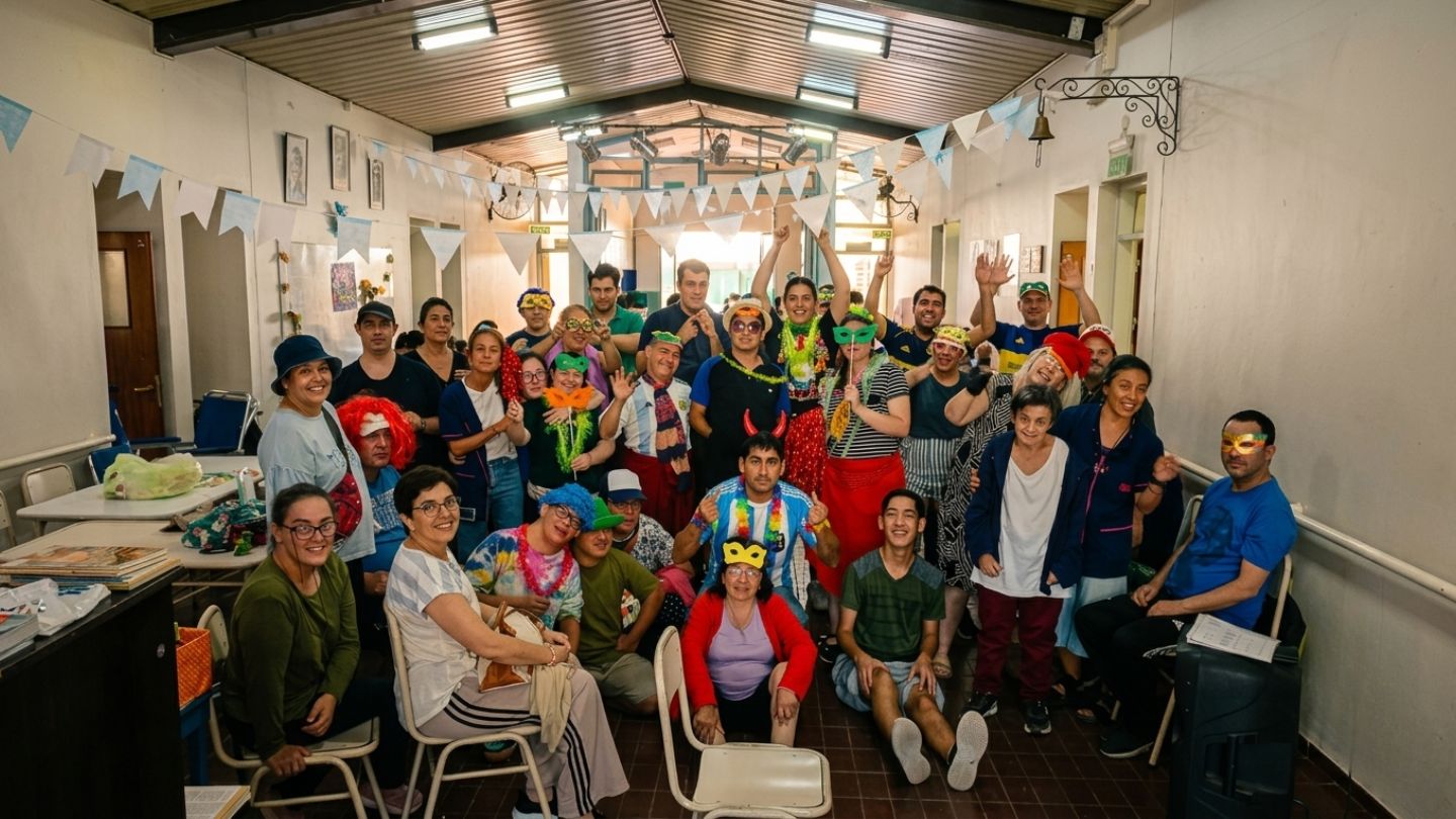 Festejo de carnaval en IPSI: alumnos y docentes posan disfrazados con antifaces y pelucas en el salón decorado con guirnaldas argentinas.