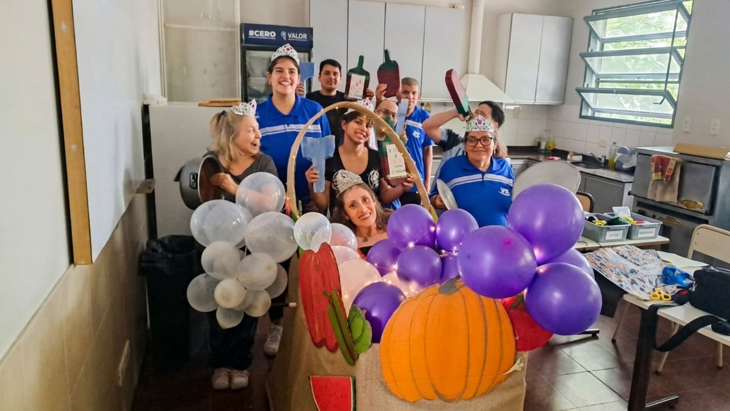 Alumnos coronados con tiaras posan en la cocina junto a una decoración temática de cosecha con globos morados y blancos y una calabaza.